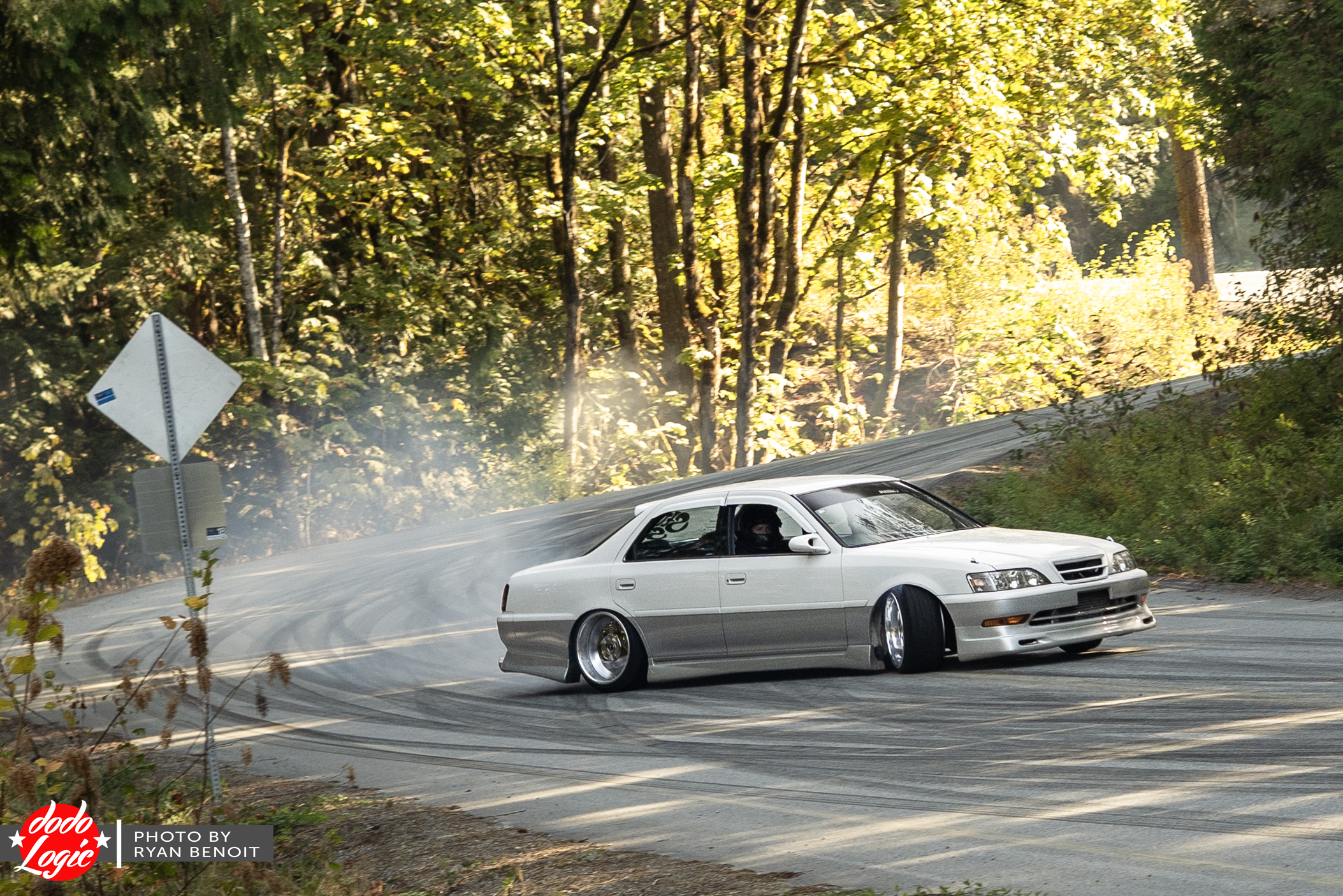 White drift car enters a mountain hairpin beneath sunlit trees