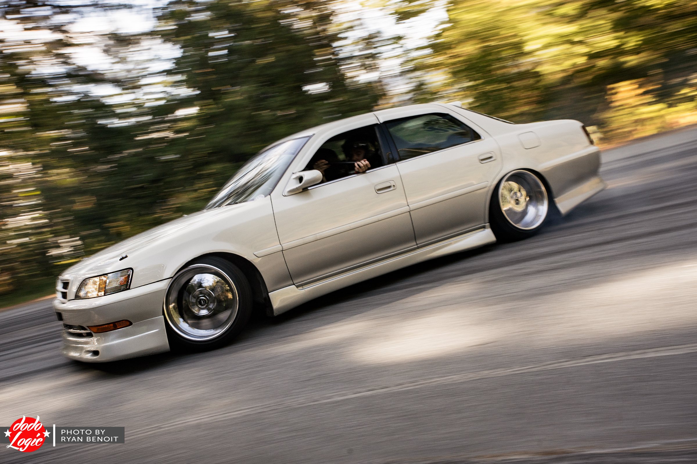 White Toyota sedan drifting through a sunlit forest bend