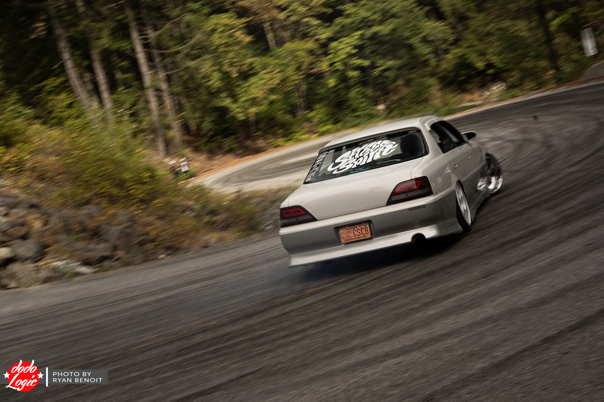Silver sedan drifting around a forested mountain road bend