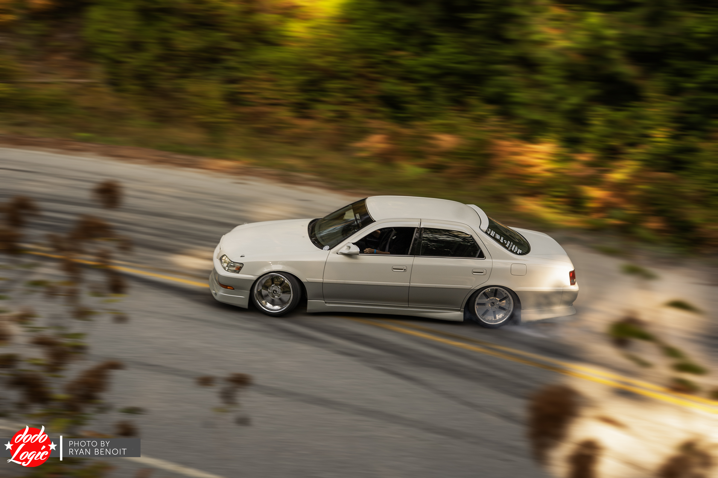 White drift car slides through a mountain bend in warm evening light